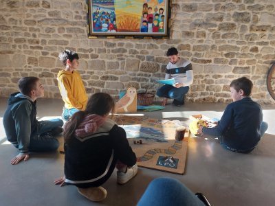 4 enfants de primaire sont assis par terre avec un animateur LPO autour d'un plateau de jeu en bois.